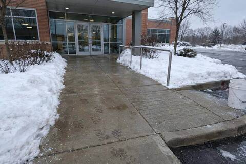 Commercial building entrance walkway and curb ramp cleared to bare concrete, ice melt granules scattered across both