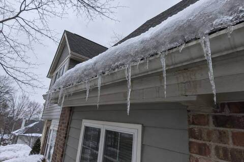 Ridge of ice built up along a roof edge above the gutter, with heavy icicles hanging from the gutter lip