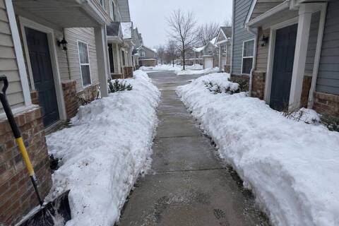 Shared concrete walkway between attached townhouse buildings, cleared at shovel width with snow banked on both sides