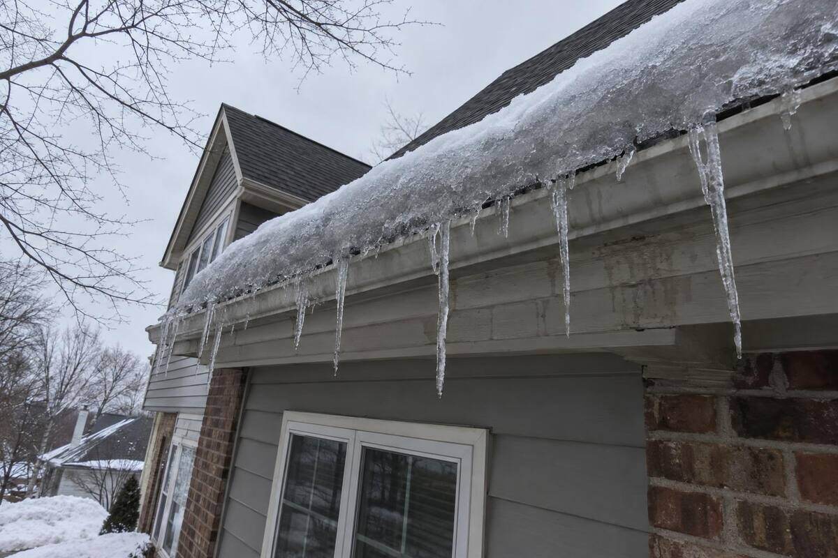 Ridge of ice built up along a roof edge above the gutter, with heavy icicles hanging from the gutter lip